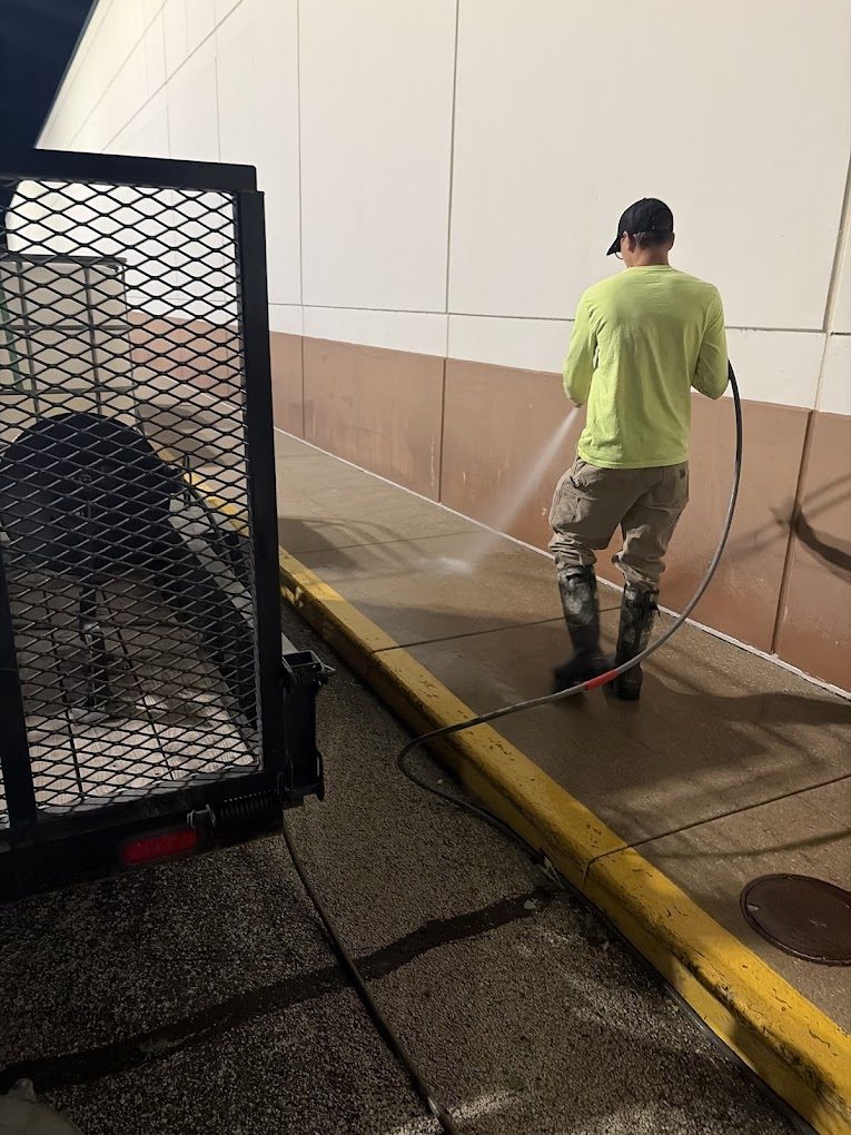 Crew member pressure washing the sidewalk along a commercial building