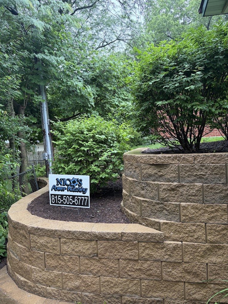 Curved stone retaining wall after cleaning, with the Nico's Power Washing sign