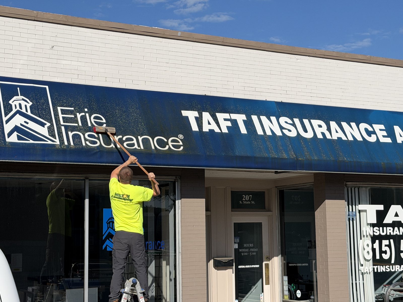 Crew member on a ladder washing storefront windows and signage